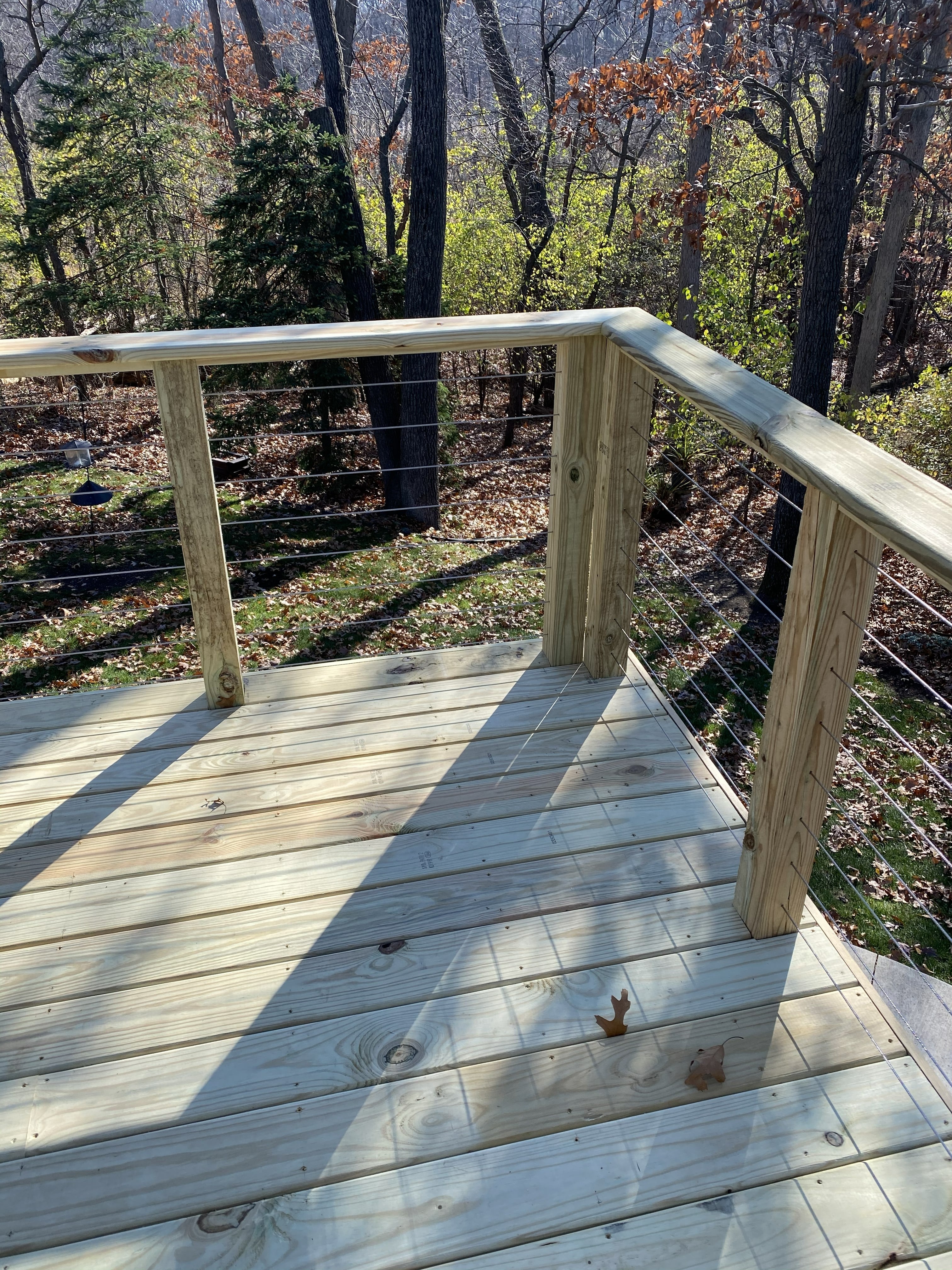 Completed pressure-treated wood deck with horizontal cable wire railing system and wooded natural backdrop by JD Contracting LLC