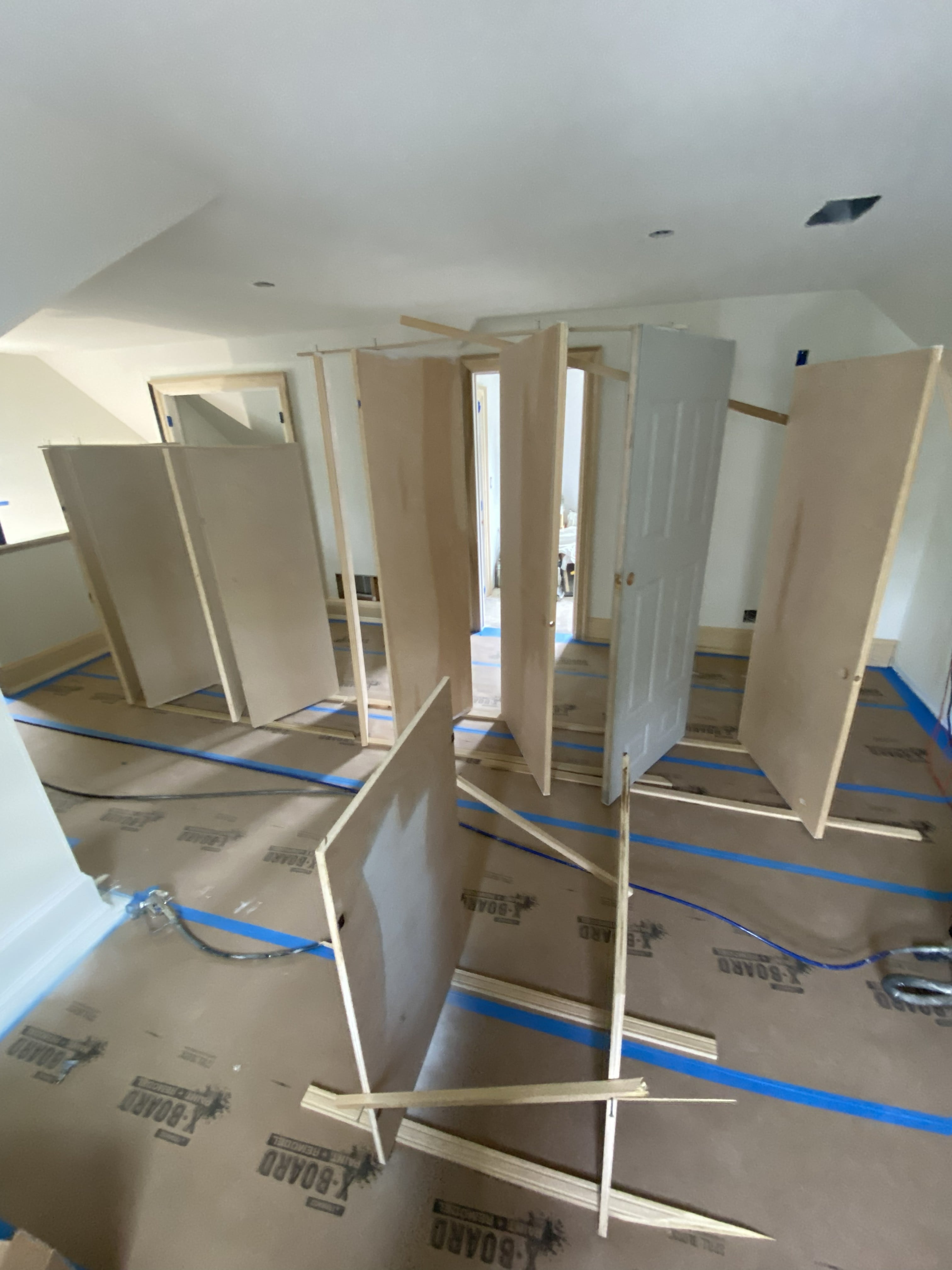Commercial asset modernization showing interior door installation with multiple hollow-core doors staged for fitting throughout an open room with floor protection, vaulted ceiling, and recessed lighting: by JD Contracting LLC