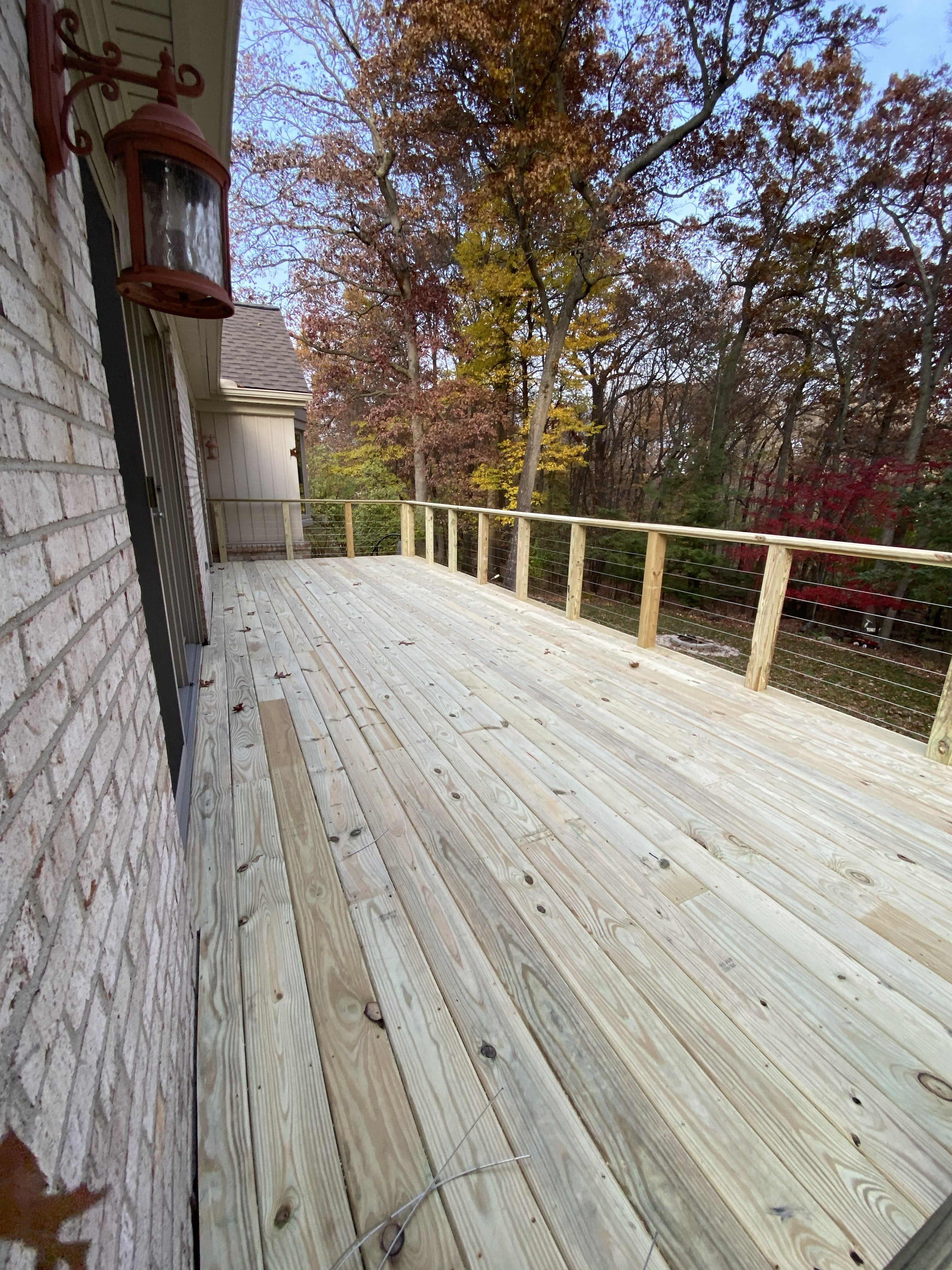 Elevated pressure-treated deck landing with cable wire railing attached to the side of a brick colonial home: rebuilt by JD Contracting LLC