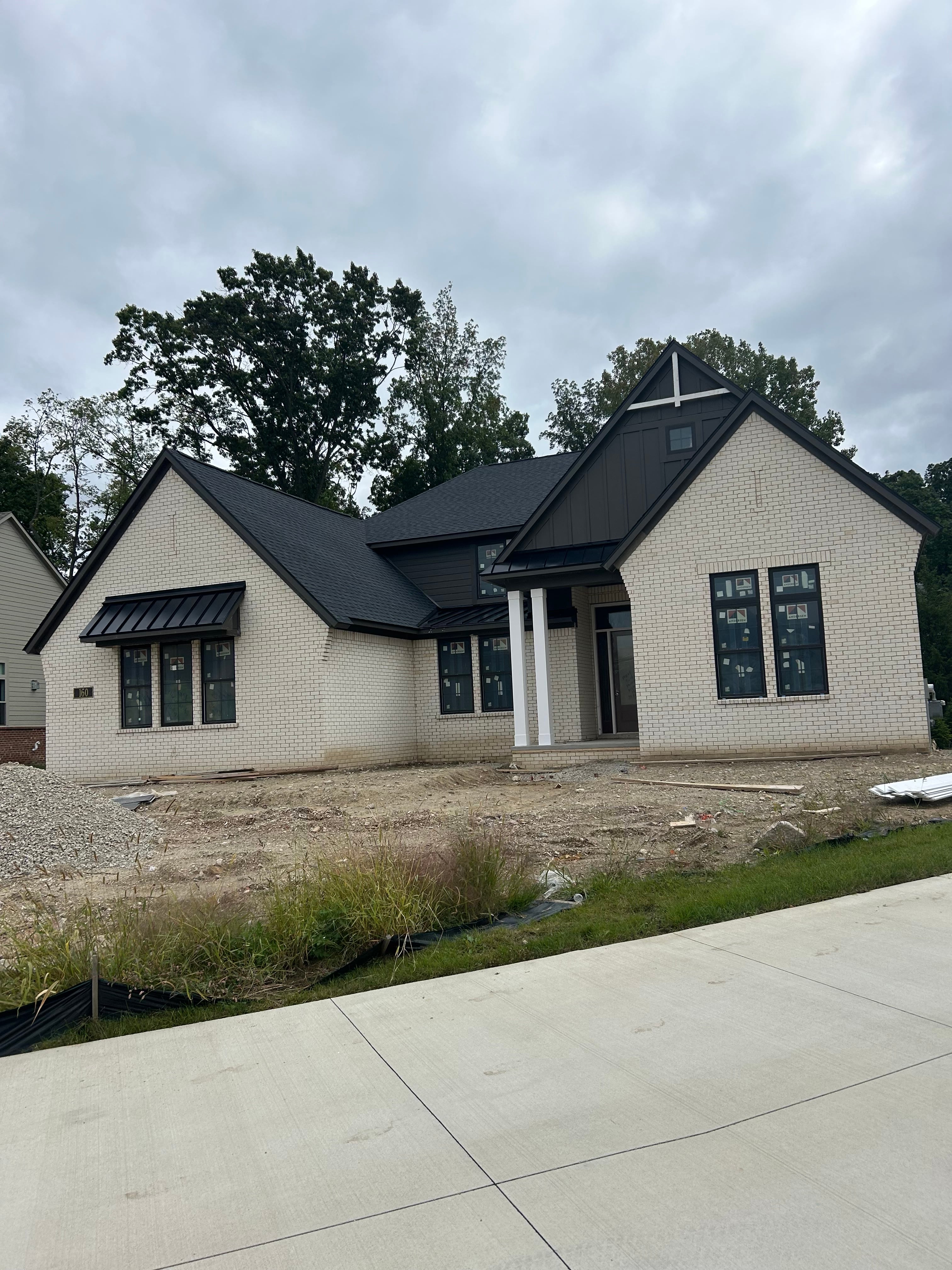 Newly completed ranch-style home with multi-gable dark charcoal asphalt shingle roof, white brick exterior, black window frames, and white column entry: roofing installation by JD Contracting LLC