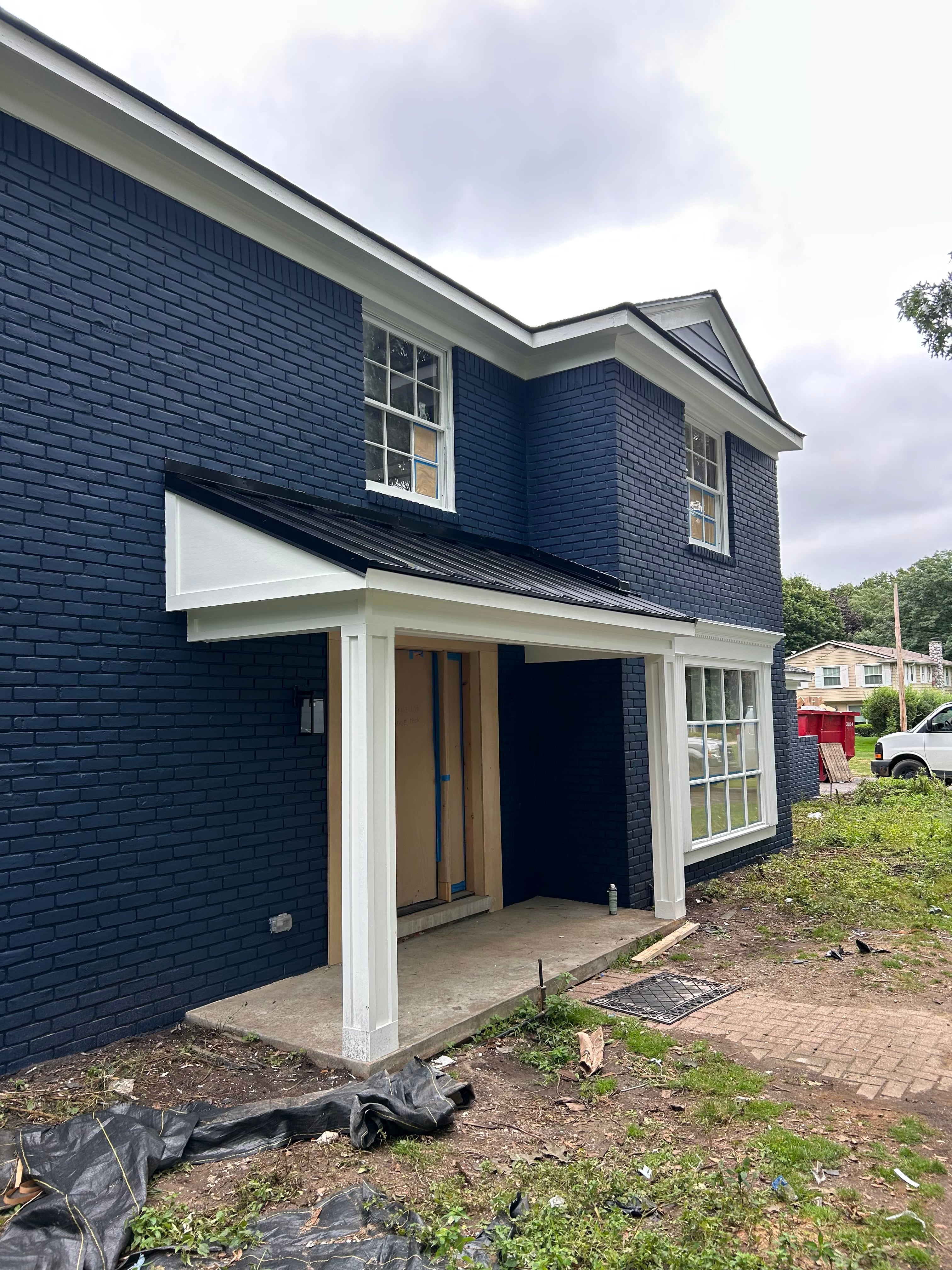 Two-story home with newly installed dark charcoal architectural shingle roofing across multi-pitched gables, white column entry and trim: roofing installation by JD Contracting LLC