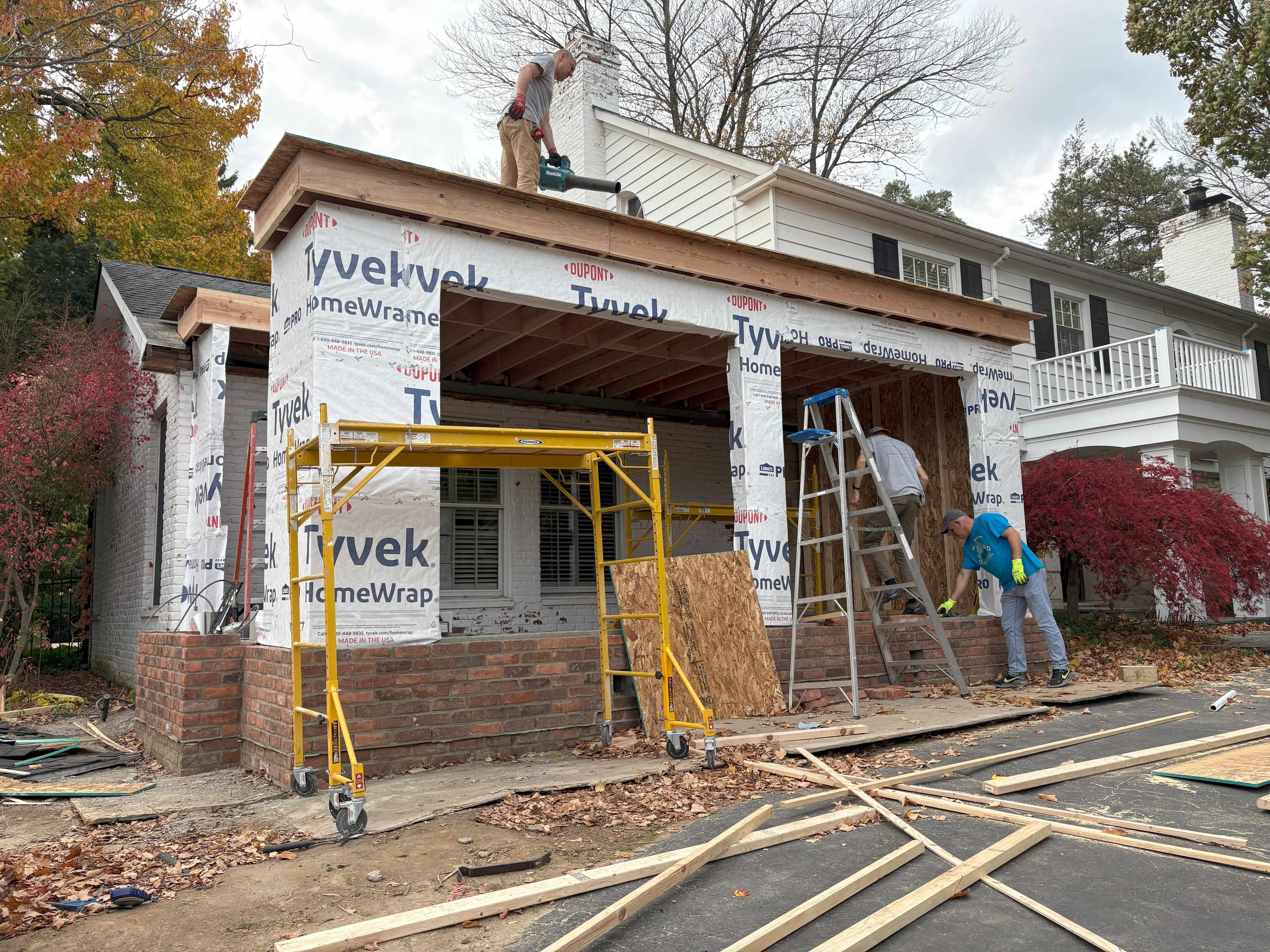Home addition framing in progress: JD Contracting crew on scaffolding installing plywood sheathing and Tyvek HomeWrap housewrap on a first-floor bump-out addition to a two-story colonial home by JD Contracting LLC