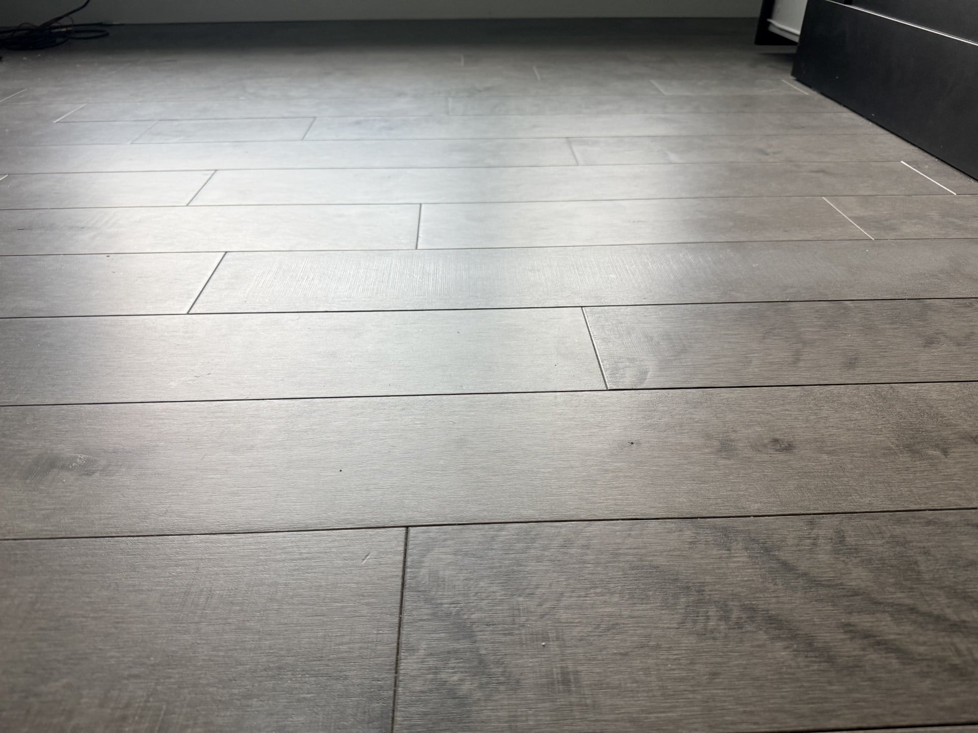 Close-up of large-format gray wood-look tile plank flooring with subtle grain texture and narrow grout lines: flooring installation by JD Contracting LLC